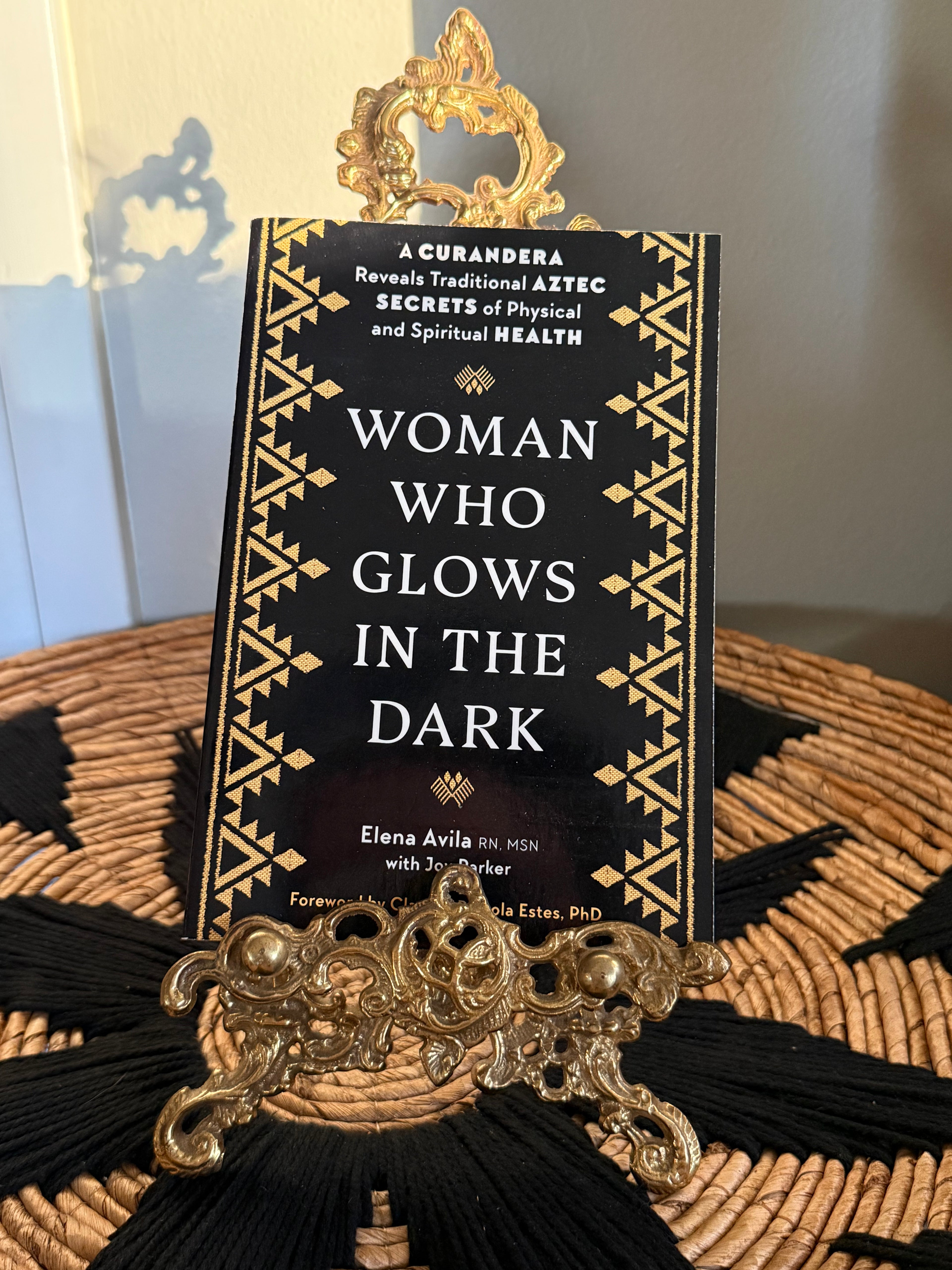 Book titled 'Woman Who Glows in the Dark' by Elena Avila on a decorative stand with a blurred background.