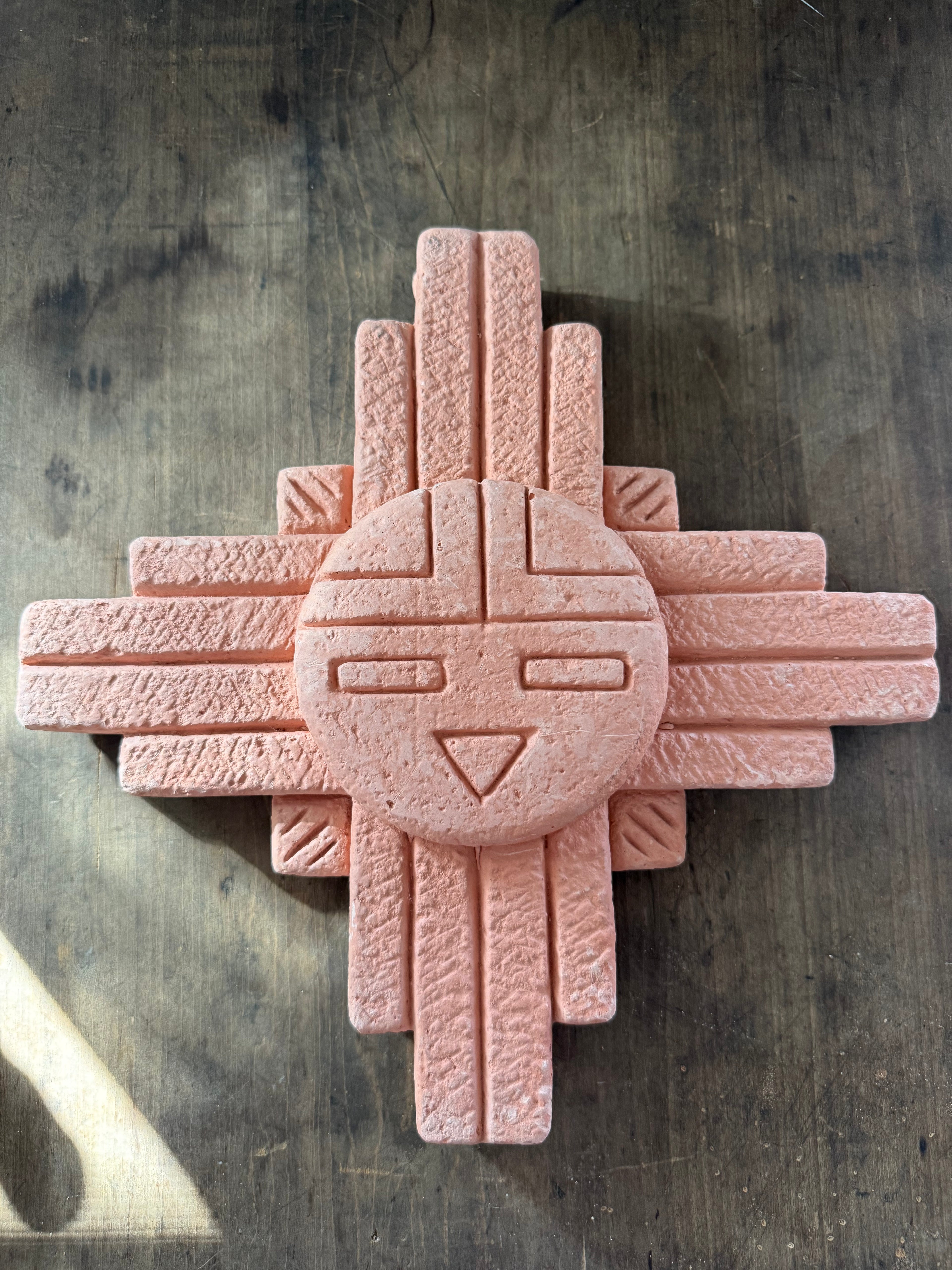 Pink stone sculpture with geometric design on a textured surface