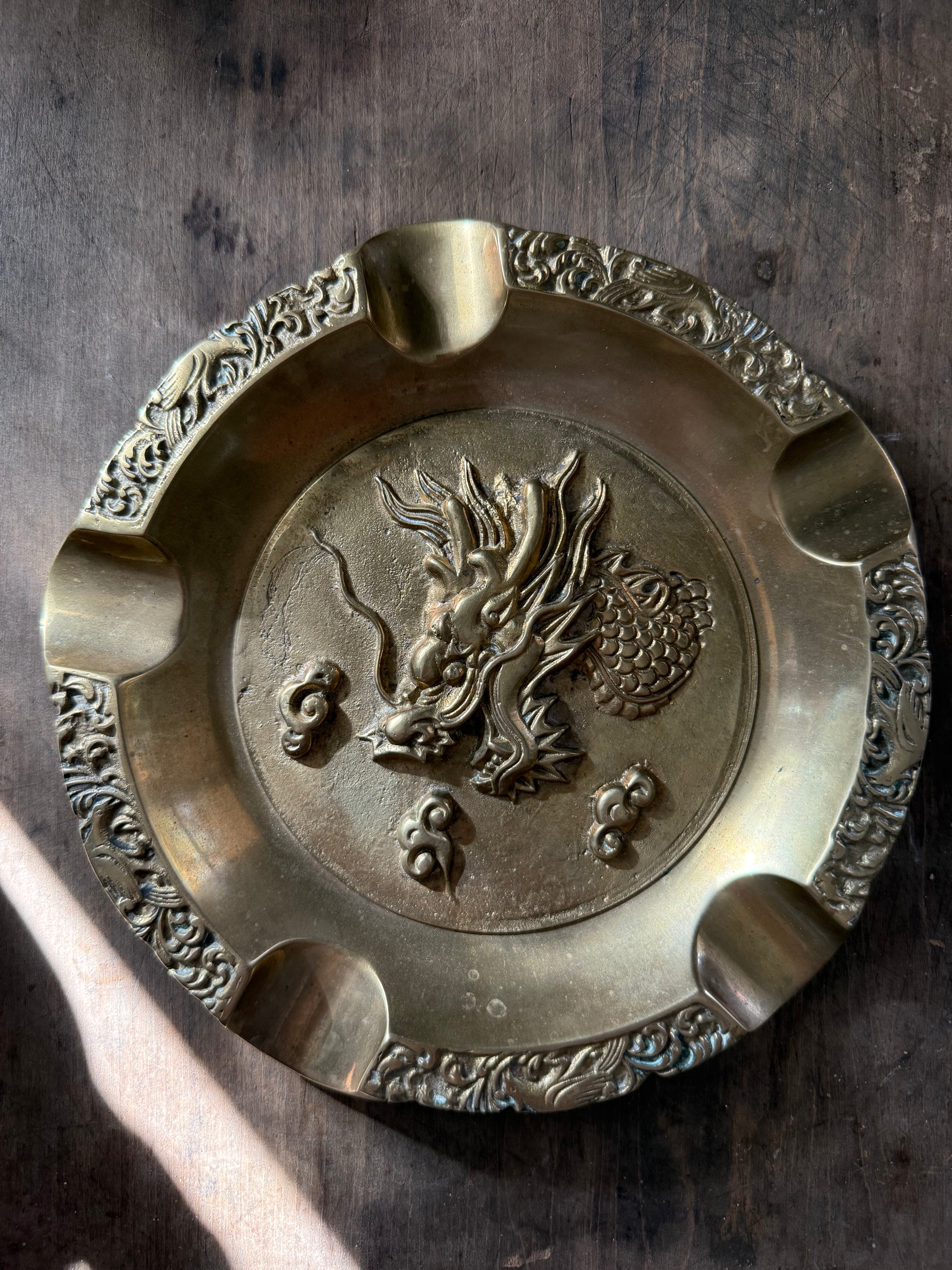 Bronze ashtray with dragon design on a wooden surface
