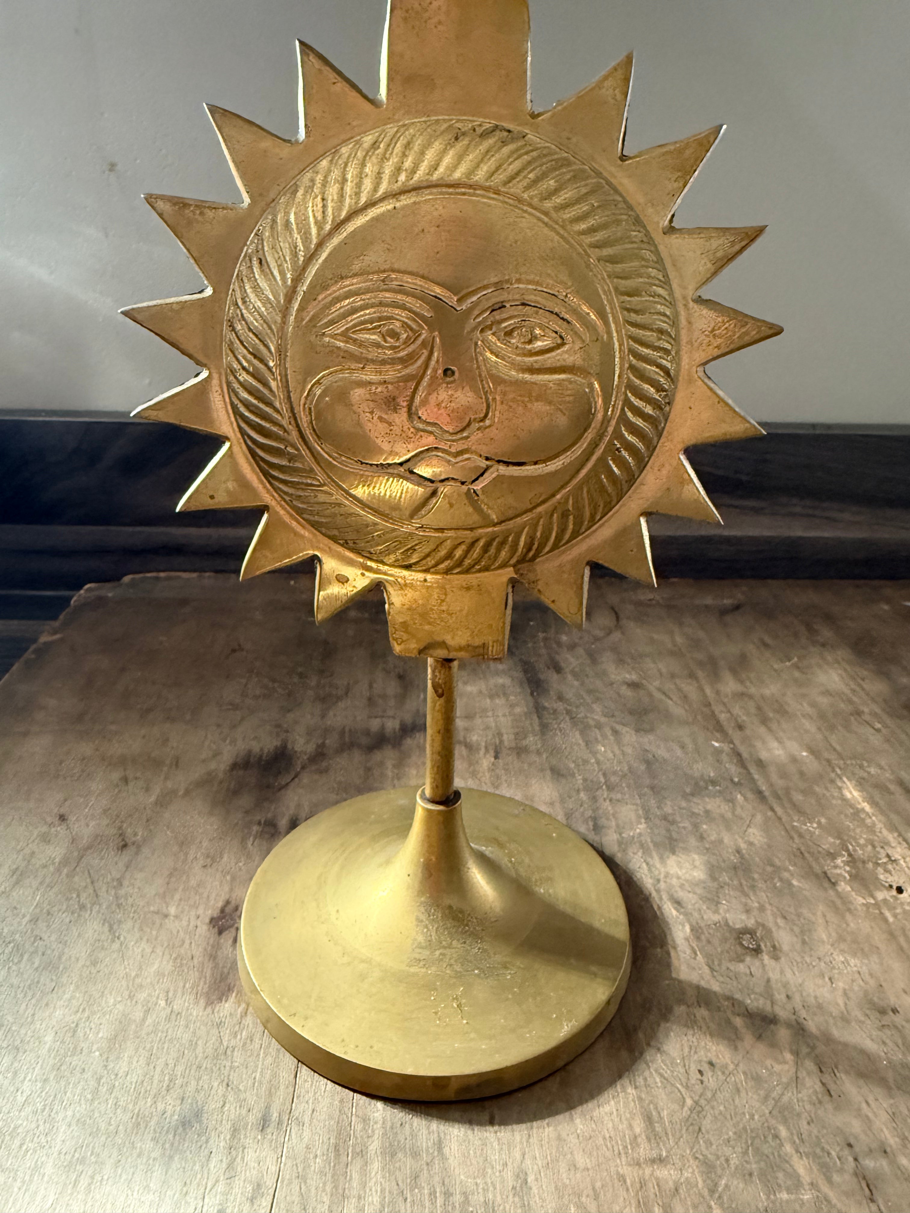 Brass sun-shaped decorative item on a stand with a neutral background