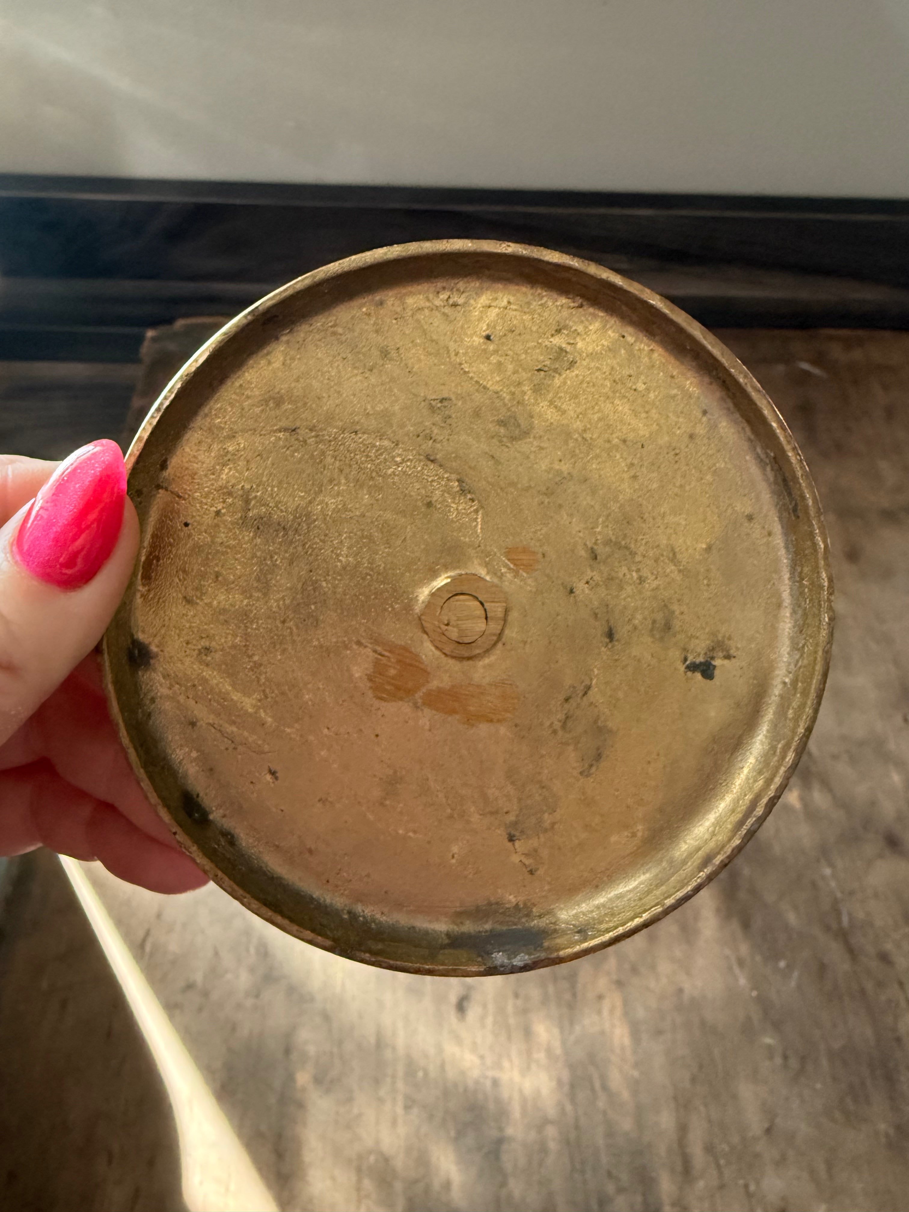 Hand holding a tarnished brass lid against a reflective surface