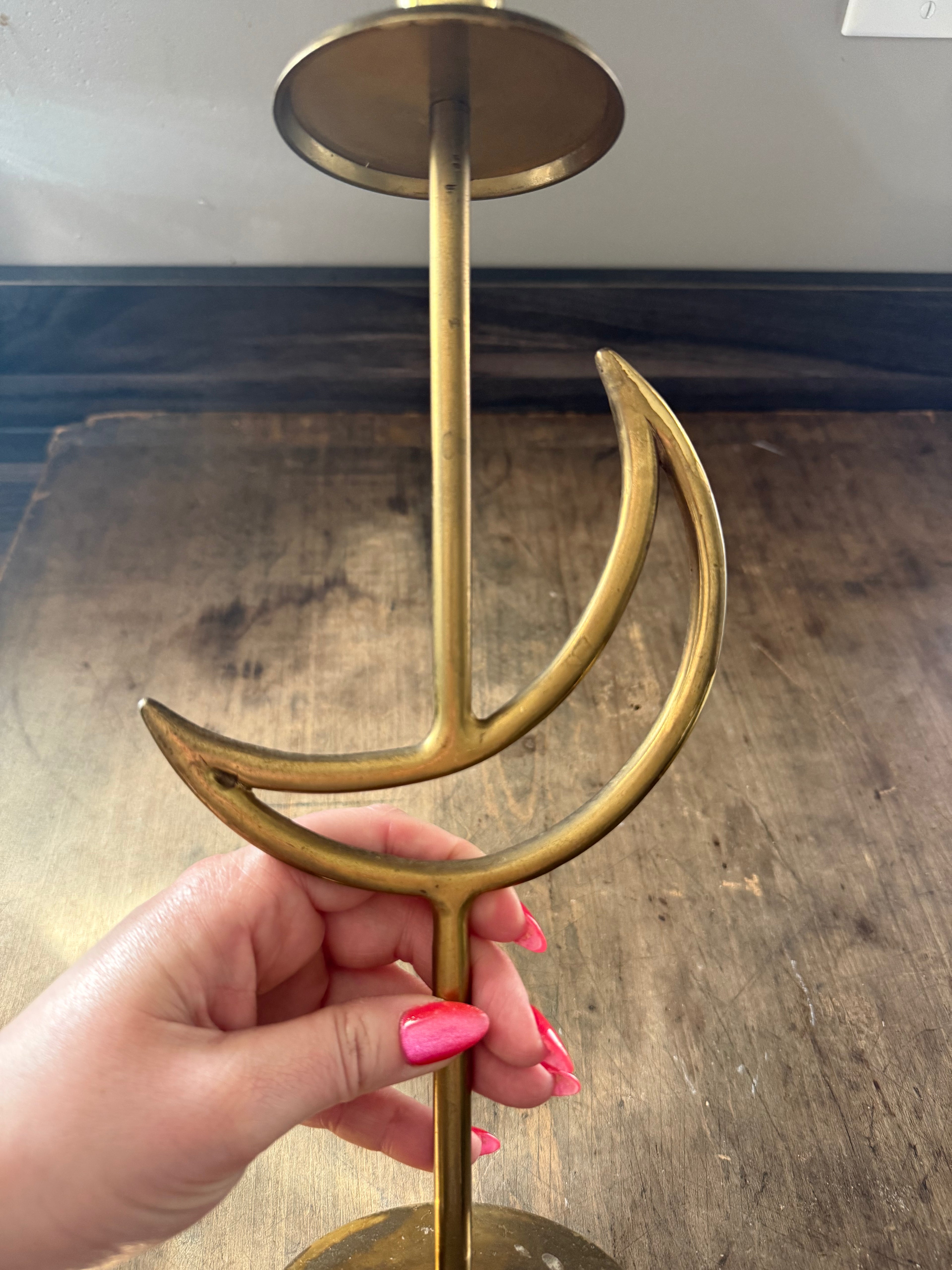 Gold anchor-shaped candle holder held by a hand on a wooden surface