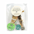 Packaged travel kit for success and prosperity with candles, sticks, and a label.