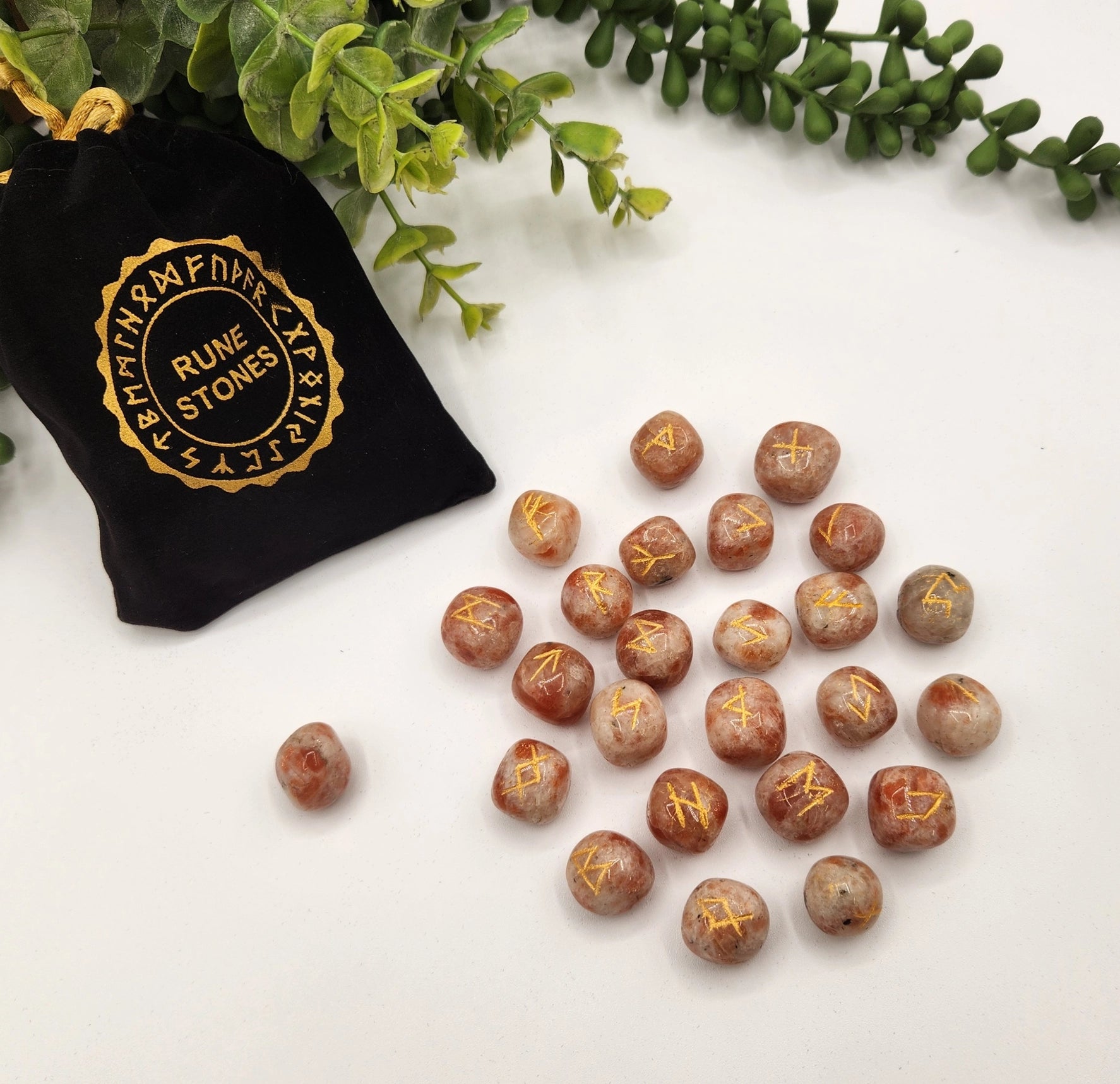 Rune stones with gold inscriptions on a white surface next to a black bag labeled 'Rune Stones'.